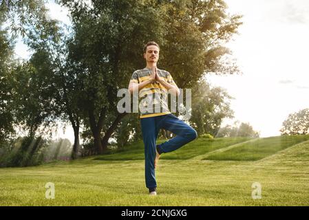 Fitness uomo che fa esercizio su una gamba isolato nel parco. Godendo natura, yoga e meditazione concetto. Spirituale pratiche.ze Foto Stock