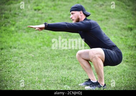 Giovane uomo attraente squatting all'aperto nel parco con le mani tese. Foto Stock