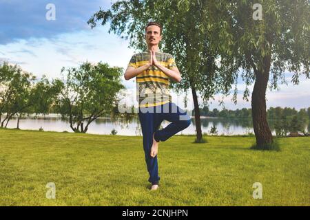 Fitness uomo che fa esercizio su una gamba isolato nel parco. Godendo natura, yoga e meditazione concetto. Spirituale pratiche.ze Foto Stock