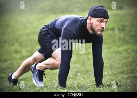 Sportivo muscolare stretching fuori prima di un allenamento sportivo presso la strada nel parco della città Foto Stock