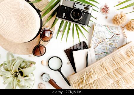 Accessori per viaggiatori su sfondo bianco con fotocamera retrò, cappello di paglia, borsa, occhiali da sole, mappa e foglia di palma tropicale. Foto Stock