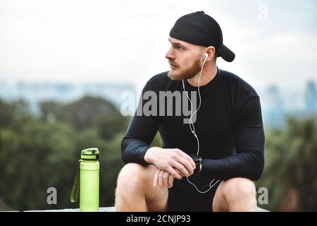 Muscolare atleta barbuto controllo calorie bruciate su smart guarda dopo una buona sessione di allenamento sul parco della città. Foto Stock