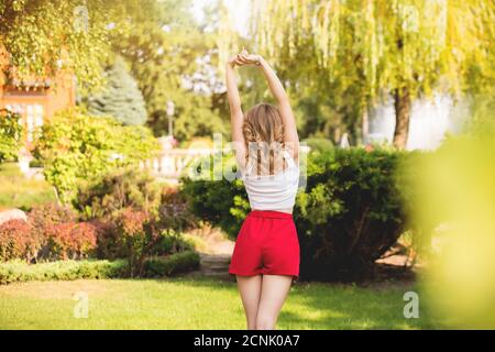 Una giovane donna in pantaloncini rossi sta in piedi con lei torna su uno sfondo naturale Foto Stock