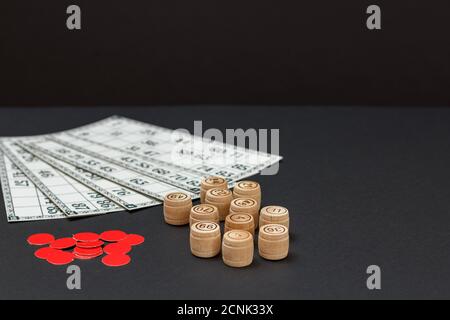 Lotto di gioco da tavolo. Botti di legno di lotto con carte di gioco e patatine rosse su sfondo nero. Foto Stock