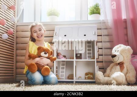 La ragazza felice gioca con la casa della bambola e l'orso del teddy a casa. Divertente, il bambino adorabile si diverte nella camera dei bambini. Foto Stock