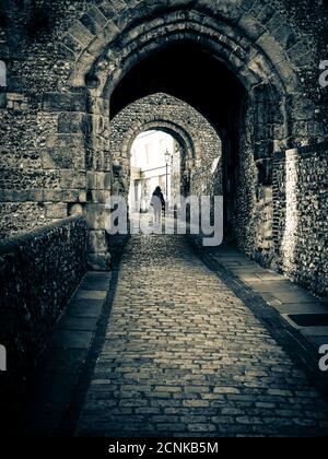 Immagine oscura e moody di una donna che cammina attraverso il sottopassaggio Barbican Gate al Castello di Lewes, East Sussex, scattato il 21st maggio 2015, in un monotone B&W. Foto Stock