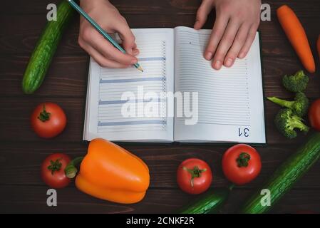 Concetto di dieta con un blocco note e penna circondato da un sacco di verdure fresche sane. Foto Stock