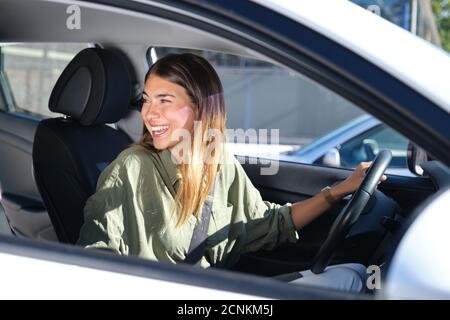 Giovane donna che guarda indietro in macchina e ride. Guida, concetti di vacanza. Foto Stock