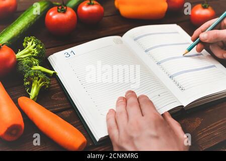 Concetto di dieta con un blocco note e penna circondato da un sacco di verdure fresche sane. Foto Stock