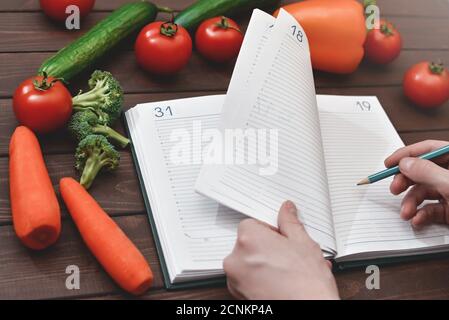 Concetto di dieta con un blocco note e penna circondato da un sacco di verdure fresche sane. Foto Stock