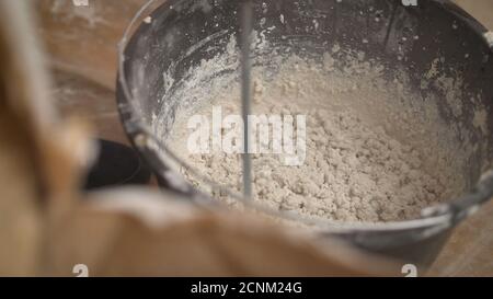 L'uomo di lavoro di costruzione agita la miscela nella costruzione della benna per l'allineamento e le pareti di stucco dell'appartamento con il aiuto di un trapano potente Foto Stock