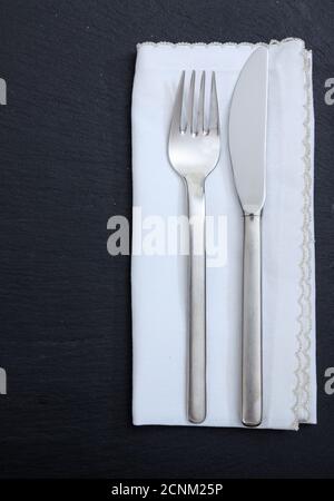 Impostazione del tavolo, pranzo di lavoro. Coltello a forchetta e tovagliolo in lino bianco isolato su sfondo nero, vista dall'alto verticale Foto Stock