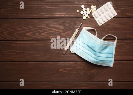 maschera protettiva medica con farmaci, termometro su sfondo di legno, spazio copia Foto Stock