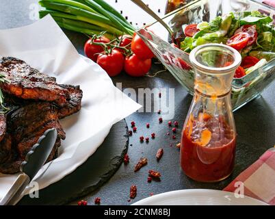 Bistecche di maiale alla griglia con salsa barbecue fatta in casa servita con fresco insalata su un tavolo da pranzo Foto Stock