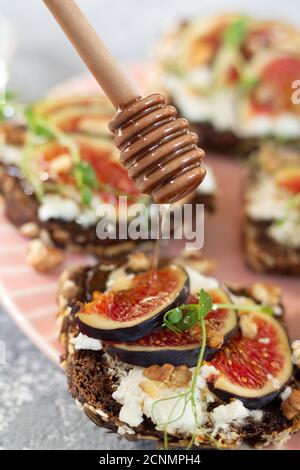 Il miele che gocciola da un gocciolatore di legno sui sandwich di fichi da vicino Foto Stock