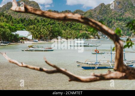 Barche da pesca ormeggiate in laguna, spiaggia sabbiosa con sfondo roccioso dell'isola vicino a El Nido sull'isola di Palawan, Filippine. Foto Stock