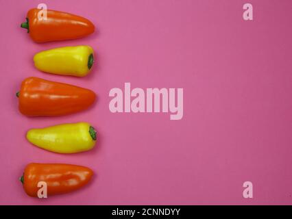 Vista sul giallo e arancio di colore rew dolce mini campana peperoni in una fila con sfondo rosa vuoto per il testo spazio di copia Foto Stock