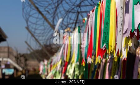 Nastri di preghiera attaccati ad una recinzione di filo spinato nella zona demilitarizzata coreana, Corea del Sud. Traduzione: 'Pace' Foto Stock