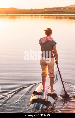 Giovane donna si levano in piedi su paddleboarding al tramonto, Lago di Wallersee, Flachgau, Salisburgo, Austria Foto Stock