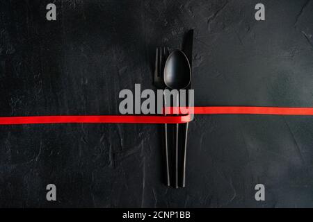 Nastro rosso legato intorno alle posate su sfondo nero Foto Stock