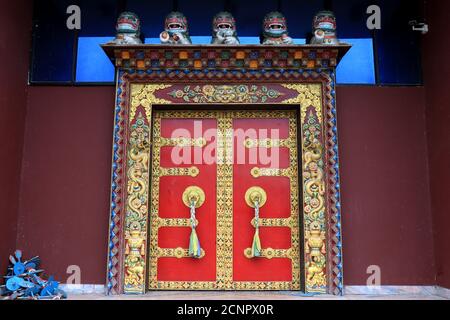 Maniglie ornate e sciarpe di preghiera sull'antico monastero del parco del Buddha a Ravangla nel sud di Sikkim, India. Porta di colore rosso al Parco Buddha di Ravangla. Foto Stock