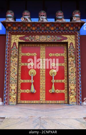 Maniglie ornate e sciarpe di preghiera sull'antico monastero del parco del Buddha a Ravangla nel sud di Sikkim, India. Porta di colore rosso al Parco Buddha di Ravangla. Foto Stock