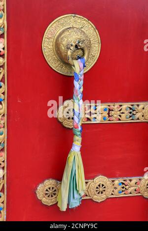 Maniglie ornate e sciarpe di preghiera sull'antico monastero del parco del Buddha a Ravangla nel sud di Sikkim, India. Porta di colore rosso al Parco Buddha di Ravangla. Foto Stock