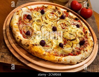 Tonno pizza italiana servita senza taglio su una tavola di legno in una cucina o pizzeria Foto Stock