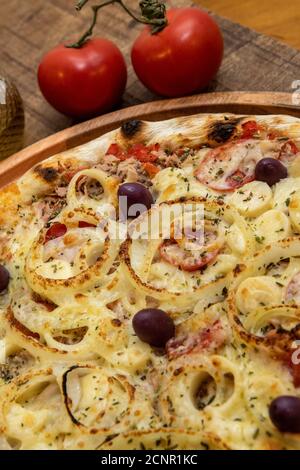 Tonno pizza italiana servita senza taglio su una tavola di legno in una cucina o pizzeria Foto Stock