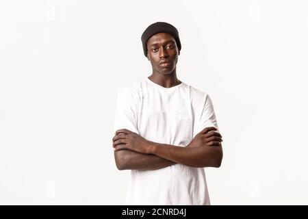 Ritratto di un giovane afro-americano, scettico e indivertito, in piedi con le braccia incrociate e fronte di poker, riluttante o indifferente Foto Stock