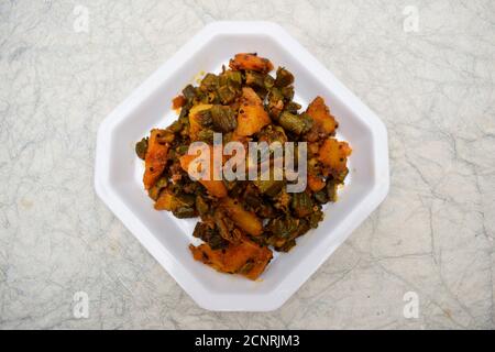 Vista dall'alto del bhindi aloo sabji o del ladyfinger okra miscelato con patate al curry vegetale indiano servito in piatto bianco su sfondo bianco. Gustoso e delizioso Foto Stock