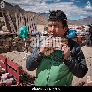 Un commerciante di mercato che dimostra panpipe panpan-pipe syrinx in un mercato stradale in Altiplano alte Andes, Perù, la vendita di tessuti e tessuti Foto Stock