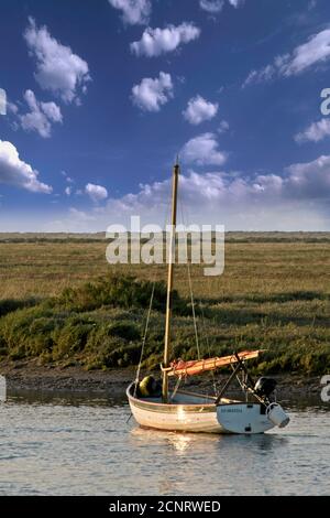 Barca a vela tradizionale a ormeggi in estuario. Soffici nuvole bianche contro un cielo blu. Burnham Overy, Norfolk. Formato verticale. Foto Stock