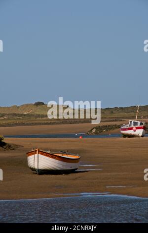 Barche ormeggiate in alto e asciutto a bassa marea su rive di sabbia di estuario. Cielo blu chiaro. Burnham Overy, Norfolk. Formato verticale. Foto Stock