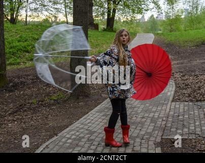 Una ragazza con due ombrelli sta girando in un vicolo del Parco. Foto Stock