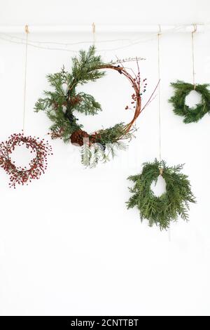 Creative corone natalizie naturali e diverse con bacche rosse e rami di abete, isolate su bianco. Buon Natale. Hangin rustico di corona di natale Foto Stock