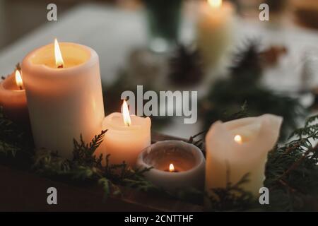 Candele brucianti su sfondo rustico con corona di natale, coni di pino e ornamenti su tavola di legno in serata. Avvenimento di laboratorio di festa, atmosfera accogliente Foto Stock
