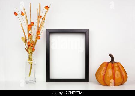 Fock up cornice nera con rami caduta e decorazione zucca su uno scaffale o scrivania. Concetto autunnale. Cornice verticale contro una parete bianca. Foto Stock