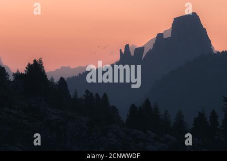 L'impressionante formazione rocciosa cinque Torri all'alba di fronte di diversi strati di catene montuose e colline in silhouette con un gregge di uccelli Foto Stock