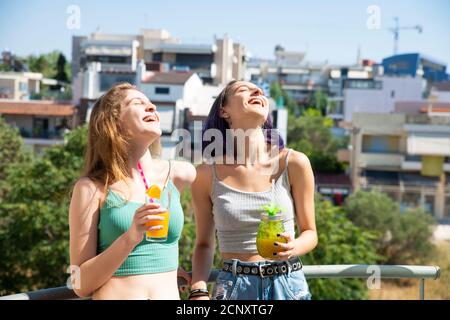 Due belle ragazze teenage che bevono succhi di frutta al balcone e la loro Laughing fuori ad alta voce. Concetto domestico Foto Stock