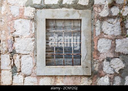 Finestra chiusa con agenti atmosferici con bar arrugginiti su una vecchia casa in pietra abbandonata sul mare. Foto Stock