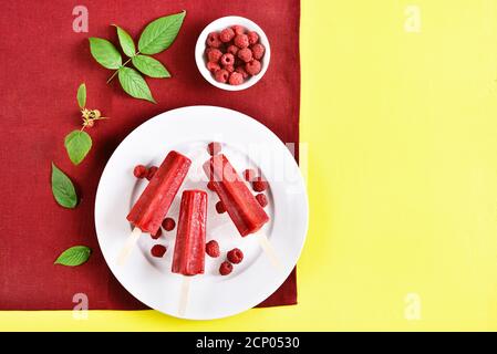 Il gelato al lampone appare su un piatto bianco su sfondo giallo con spazio di testo libero. Gustoso dessert estivo. Vista dall'alto, disposizione piatta Foto Stock