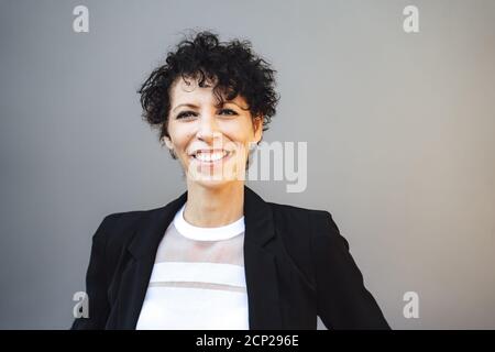 Primo piano ritratto di sorridente donna d'affari matura in vestito contro sfondo grigio Foto Stock