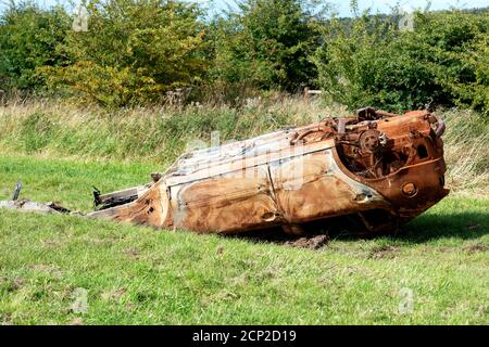 Rubato bruciato auto arrugginita abbandonato su un prato in un countriside inquinare l'ambiente Foto Stock