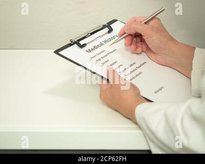 Una donna caucasica che compila un modulo di anamnesi medica su una clipboard. Profondità di campo poco profonda. Foto Stock