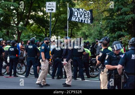 Un protestore fa ondere una grande bandiera Black Lives Matter, mentre gli ufficiali della NYPD monitorano una dimostrazione contro l'immigrazione e l'applicazione doganale a New York il 18 settembre 20202. Per un terzo giorno di fila, i manifestanti hanno dimostrato contro presunte accuse che un medico ha perfomed isterectomies medicalmente inutili su donne non documentate nella custodia di I.C.E.. (Foto di Gabriele Holtermann/Sipa USA) Credit: Sipa USA/Alamy Live News Foto Stock