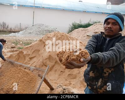 DISTRETTO KATNI, INDIA - 18 DICEMBRE 2019: Un lavoro maschile villaggio indiano che offre sabbia a macchina fotografica per la fotografia nel sito di costruzione casa. Foto Stock