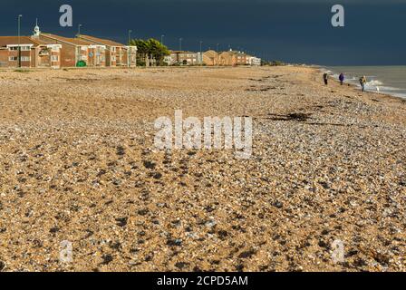 Nuvole buie tempeste che si avvicinano al mare con luce solare che illumina la spiaggia di ghiaia, che è quasi deserta, in Inghilterra, Regno Unito. Foto Stock