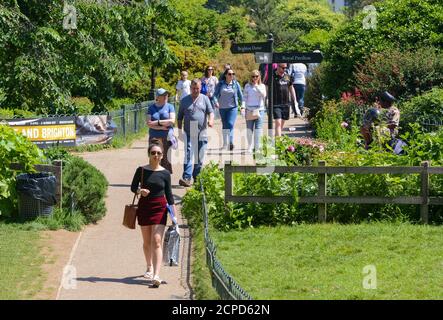 Folle di persone che camminano attraverso il parco presso i Royal Pavilion Gardens in una calda giornata estiva a Brighton, East Sussex, Inghilterra, Regno Unito. Foto Stock