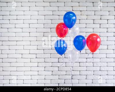 Palloncini luminosi rosso, blu e bianco messi insieme sul lato destro vicino a muro di mattoni bianchi sullo sfondo. CopySpace per il testo. 4 luglio, Inde Foto Stock